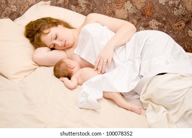 Mother Is Breast Feeding A Newborn Baby Lying Down In Bed. The Symbol Of Happiness And Motherhood