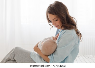 A mother is breastfeeding a baby sitting on a light window background. mother breast feeding and hugging her baby boy