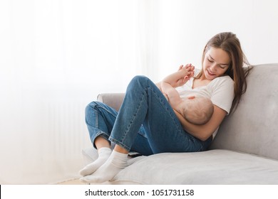 Mother is breastfeeding her kid sitting against light window background. Mom is suckling baby boy at home