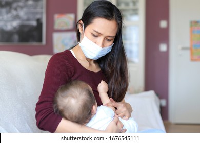 Mother Breastfeeding Her Newborn Baby In Her Arms While Wearing Surgical Face Mask Sick Concept During Corona Virus, Covid-19 Pandemic Or Allergy. Asian Mommy Sickness With Child.