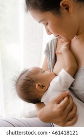 Mother breastfeeding her newborn baby beside window. Milk from mom’s breast is a natural medicine for children.