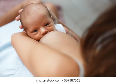 Mother breastfeeding her newborn baby beside window. Milk from mother's breast is a natural medicine to baby. Mother day bonding concept with newborn baby nursing.. Nursery interior