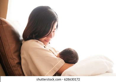 Mother breastfeeding her newborn baby beside window. Milk from mother's breast is a natural medicine to baby. Mother day bonding concept with newborn baby nursing.