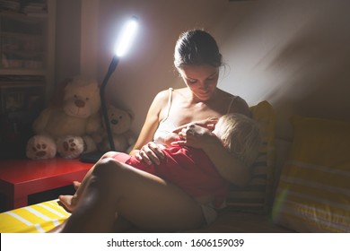 Mother, Breastfeeding Her Toddler Boy At Home At Night, Night Stand Lamp Turned On, Mom And Baby Hugging