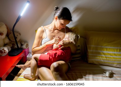 Mother, Breastfeeding Her Toddler Boy At Home At Night, Night Stand Lamp Turned On, Mom And Baby Hugging