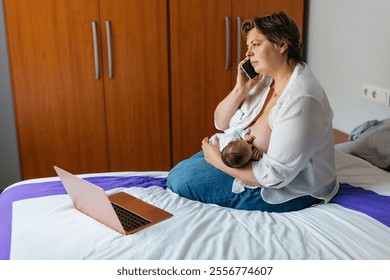 Mother breastfeeding newborn baby while talking on phone and working from home - Powered by Shutterstock