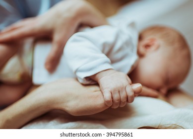 mother breastfeeds her infant , the baby holds hand of mother's hand