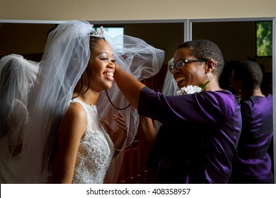 Mother of the bride adjusts her daughter's veil on her wedding day.  Beautiful, African American women, smiling while getting the daughter ready for her wedding.
