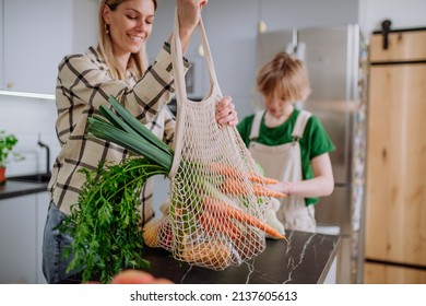 Mother bringing shopping in mesh bag to kitchen. Zero waste and sustainable packaging concept.
