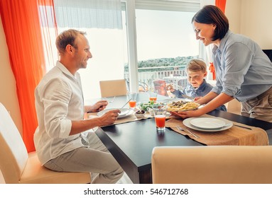 Mother brings a dish of meal at table to her hungry family - Powered by Shutterstock