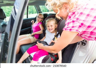 Mother buckling up on child in car safety seat 