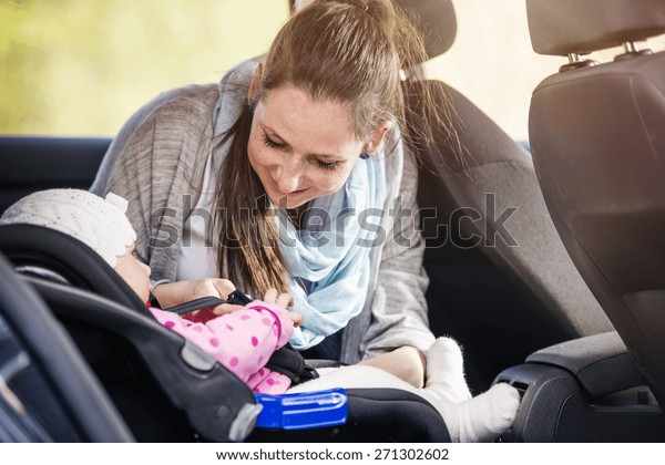Mother in a car, having her little baby girl in a\
child seat