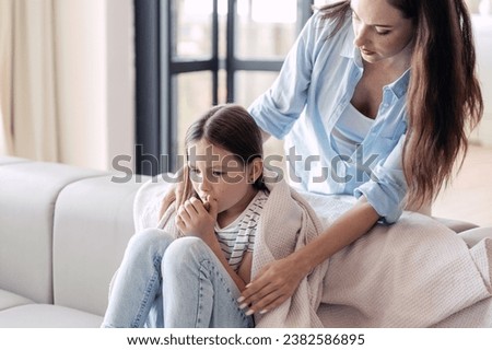 Mother care about her sick daughter, give plaid for warm. Preteen girl sitting on sofa, feeling unwell and has cough. Kid with fever and influenza symptoms. Healthcare concept