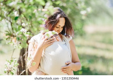 Mother carry baby girl in wrap sling in park. Summertime. Concept of natural parenting, babywearing in sling