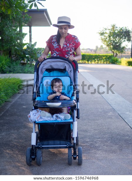 Mother carry the baby stroller along the garden\
in the evening.