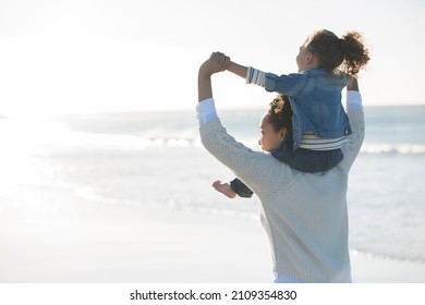 Mother Carrying Daughter On Her Shoulders On Beach