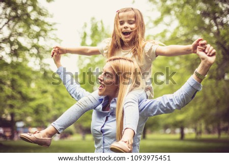 Mother carrying daughter on shoulders and spending time in park.