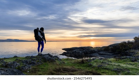 A mother carrying her baby in a backpack stands on the rocky coast of Vancouver Island, Canada, admiring a tranquil sunrise over the ocean. A serene moment of nature and family bond. - Powered by Shutterstock