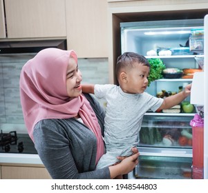 Mother Carrying Her Son And Open The Fridge Looking For Sweets Treat