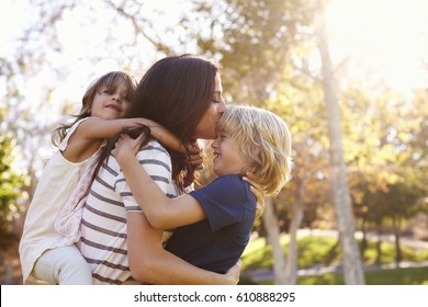 Mother Carrying Son And Daughter As They Play In Park