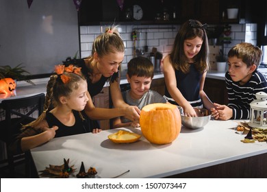 Mother Carving Halloween Pumpkin With Children At Decorated Home Kitchen