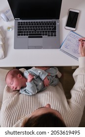 Mother With Caucasian Newborn Working At Home With A Laptop And Baby Items On The White Table.