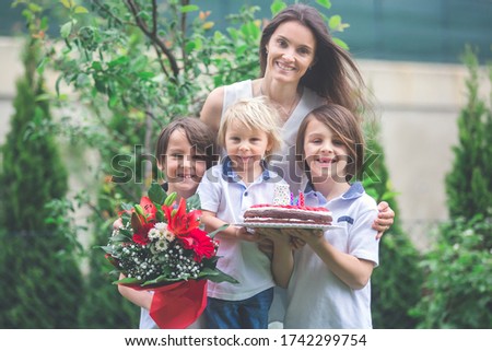 Mother, celebrating birthday with her children, holding cake and flowers in the park