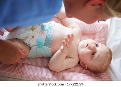 Mother Changing Baby Son's Nappy As He Lies On Mat