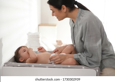 Mother changing baby's diaper on table at home - Powered by Shutterstock