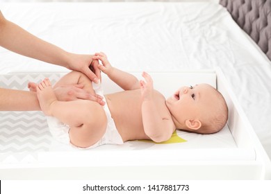 Mother Changing Her Baby's Diaper On Table Indoors