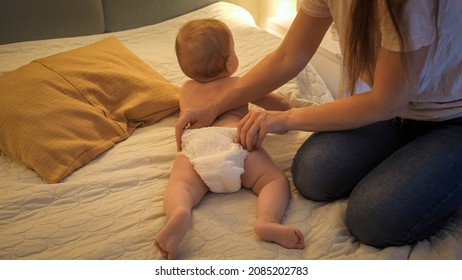 Mother Changing Messy Used Diapers To Her Baby Son At Night. Concept Of Children Hygiene, Healthcare And Family Care At Home