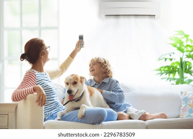 Mother and child with air conditioner remote control. Comfortable temperature at family home. Cooling and heating device. Mom and kid on couch under cold breeze. Air conditioning on hot summer day.  - Shutterstock ID 2296783509