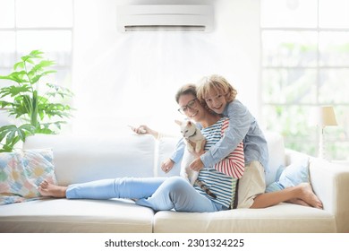 Mother and child with air conditioner remote control. Comfortable temperature at family home. Cooling and heating device. Mom and kid on couch under cold breeze. Air conditioning on hot summer day.  - Shutterstock ID 2301324225