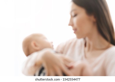 Mother and child background. Blurred image of young woman holding her cute infant baby in arms, free space