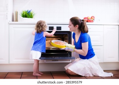 Mother And Child Bake A Pie. Young Woman And Her Daughter Cook In A White Kitchen. Kids Baking Pastry. Children Helping To Make Dinner. Modern Interior With Oven And Other Appliances. Family Eating.