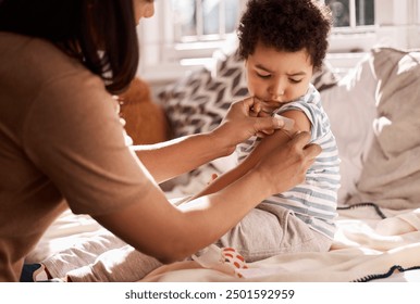 Mother, child and bandage on arm with injury for wound treatment, helping and care for bruise on bed in home. First aid, woman and apply adhesive plaster on son in bedroom with accident and support - Powered by Shutterstock