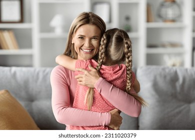 Mother Child Bonding. Happy Mom Embracing Her Little Daughter At Home, Loving Mommy Hugging Tight Female Kid And Smiling At Camera While Relaxing Together In Living Room Interior, Copy Space - Shutterstock ID 2311020379