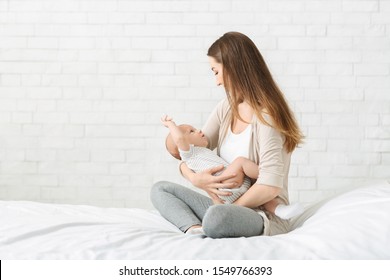 Mother And Child Connection. Millennial Mom Sitting On Bed With Newborn Baby In Arms