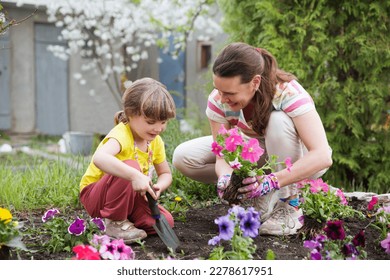 mother and child daughter plant flowers in the garden near the houme on spring day. Kid help mom work in the garden. slow life. enjoy the little things.  - Powered by Shutterstock