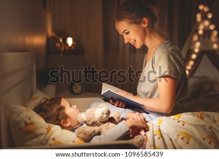 mother and child daughter reading book in bed before going to sleep 

