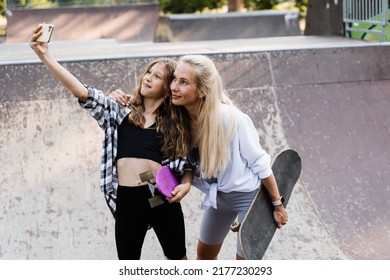 Mother And Child Daughter With Skate And Penny Board Is Making Selfie On Phone In Skate Park. Extreme Lifestyle. Family Of Mom And Her Kid Spend Time Together