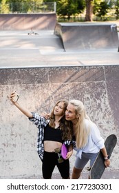 Mother And Child Daughter With Skate And Penny Board Is Making Selfie On Phone In Skate Park. Extreme Lifestyle. Family Of Mom And Her Kid Spend Time Together