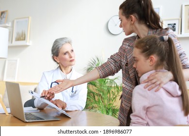 Mother And Child In The Doctor Office Meeting The Pediatrician, They Are Sitting At Desk In Hospital