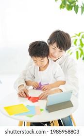 Mother And Child Doing Origami While Looking At A Tablet PC