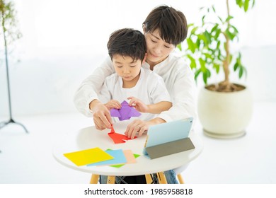 Mother And Child Doing Origami While Looking At A Tablet PC