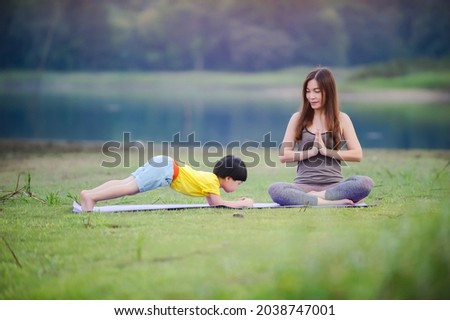 Mother and child doing yoga exercises on grass at the park befor sunset in summer.