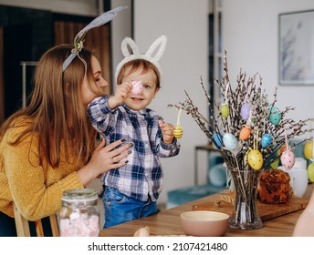 Mother and child draw on Easter eggs and hang them on branches. Preparation of decorations for Easter in the home interior - Shutterstock ID 2107421480