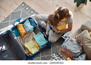 Mother And Child Embrace And Pack Things In A Suitcase Together. Family Relocation, Flight From The Country, Closed Borders