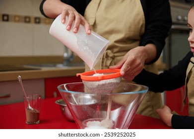 A mother and child enjoy baking together in their home kitchen, sifting flour for a recipe. The bonding moment captures family, baking, and cooking concepts with a warm and cozy atmosphere. - Powered by Shutterstock