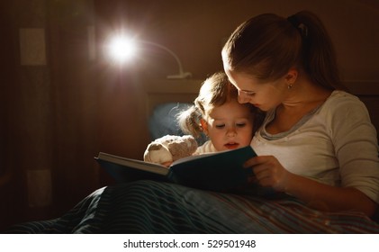 Mother And Child Girl Reading A Book In Bed Before Going To Sleep